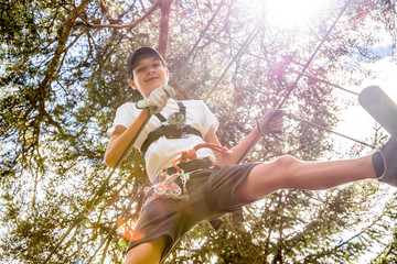 Teenager with action camera having fun on high ropes course, adventure park, climbing trees in forest in summer