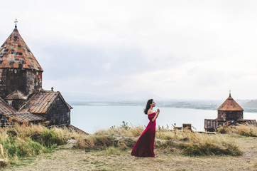 Wall Mural - Portrait of young woman in red dress standing near monastery and pray, Armenia