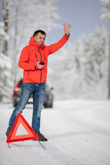 Handsome man setting up a warning triangle and calling for assistance after his car broke down in the middle of nowhere on a freezing winter day