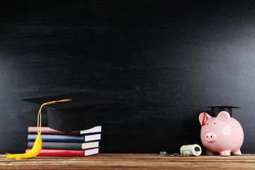 Wall Mural - Piggybank with graduation cap, books and money on blackboard background