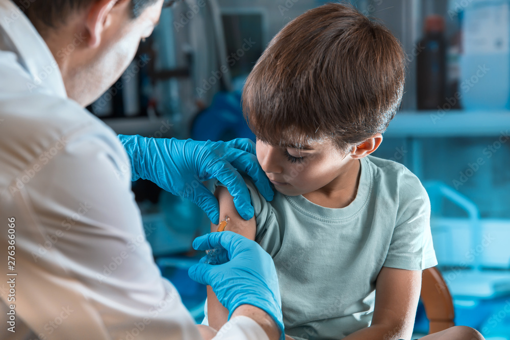 pediatrician vaccinating little boy in the pediatric clinic / doctor holding syringe subcutaneous vaccine for child in the medical office  - obrazy, fototapety, plakaty 