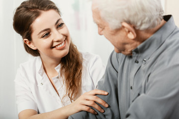 Wall Mural - Beautiful volunteer smiling at senior man at nursing home