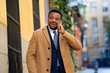 © SB Arts Media - Portrait of handsome african american businessman walking in the city talking on mobile phone