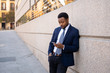© SB Arts Media - Young handsome businessman using mobile phone app sending message outside office in urban city