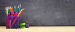 © Jenifoto - School supplies on a wood desk with chalkboard background. Side view. Back to school concept. Copy space. Banner orientation.