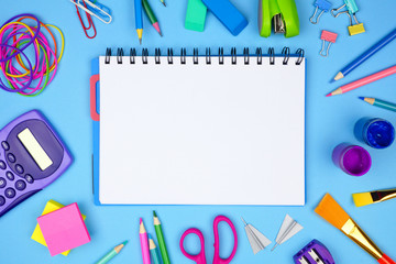 Wall Mural - Blank coil notebook with school supplies frame against a blue background. Back to school concept. Copy space.
