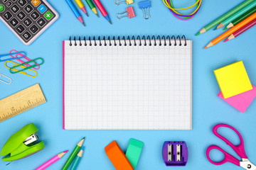 Wall Mural - Blank graphing paper notebook with school supplies frame against a blue background. Back to school concept. Copy space.