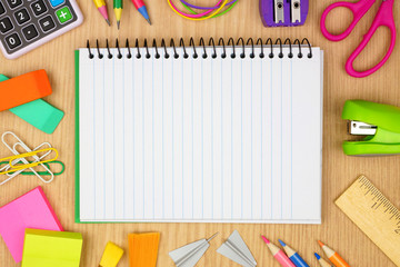 Wall Mural - Blank, lined, coil notebook with school supplies frame against a wood desk background. Back to school concept. Copy space.