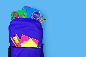 Wall Mural - Purple backpack full of school supplies against a blue background. Close up, top view with copy space.