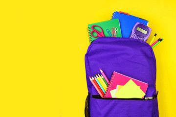 Wall Mural - Purple backpack full of school supplies against a bright yellow background. Close up, top view with copy space.