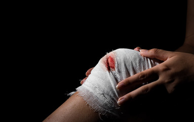 Injured knee with white bloody gauze bandage on dark black background