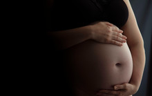 Pregnant Woman Holding A Baby Bump Against A Dark Background
