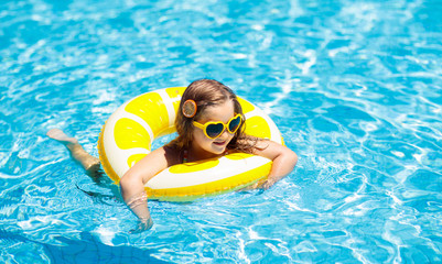 Child in swimming pool on ring toy. Kids swim.