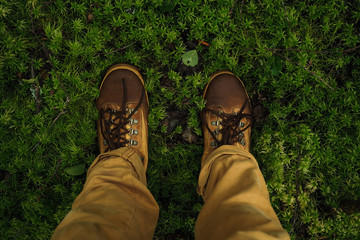 POV legs standing on beautiful green moss in brown pants and wet hikers