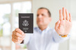 © Krakenimages.com - Middle age man holding holding passport of United States with open hand doing stop sign with serious and confident expression, defense gesture