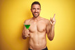 © Krakenimages.com - Young handsome shirtless man drinking a summer cocktail over isolated yellow background very happy pointing with hand and finger to the side