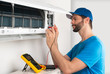 © stockphoto-graf - Installation service fix repair maintenance of an air conditioner indoor unit, by cryogenist technican worker with multimeter checking electric blue shirt baseball cap