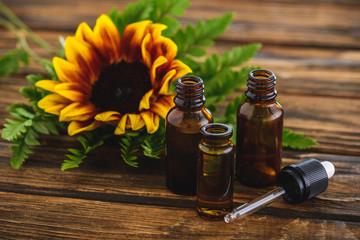 Wall Mural - sunflower, fern leaves, bottles with essential oils and dropper on wooden surface