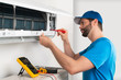 © stockphoto-graf - Installation service fix  repair maintenance of an air conditioner indoor unit by cryogenist technican worker with screwdriver  blue shirt baseball cap