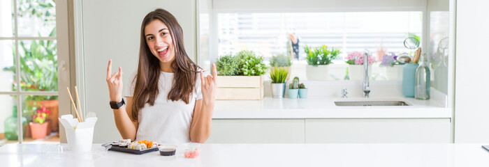 Sticker - Wide angle picture of beautiful young woman eating asian sushi from delivery shouting with crazy expression doing rock symbol with hands up. Music star. Heavy concept.