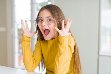 Wall Mural - Beautiful young girl kid wearing glasses celebrating crazy and amazed for success with arms raised and open eyes screaming excited. Winner concept