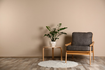 Poster - Stylish room interior with comfortable armchair and plant near color wall. Space for text