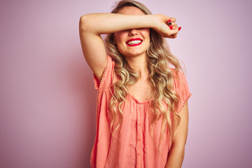 Young beautiful woman wearing t-shirt standing over pink isolated background covering eyes with arm smiling cheerful and funny. Blind concept.