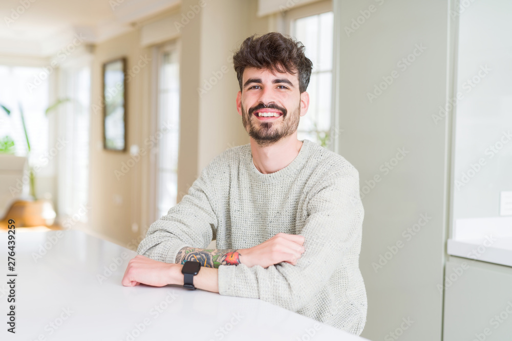 Young man wearing casual sweater sitting on white table with a happy and cool smile on face. Lucky person.