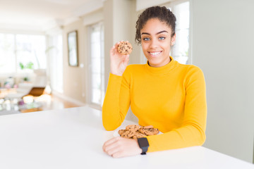 Young african american girl eating chocolate chips cookies as sweet snack with a happy face standing and smiling with a confident smile showing teeth