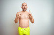 © Krakenimages.com - Young shirtless man on vacation wearing yellow swimwear over isolated background amazed and surprised looking up and pointing with fingers and raised arms.