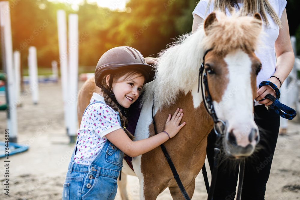 Cute little girl and her older sister enjoying with pony horse outdoors at ranch. - obrazy, fototapety, plakaty 