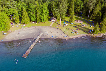 Aerial photo of Cultus Lake in Chilliwack, B.C. while people are enjoying the summer activities at the lakeshore and doing barbeque in the woods by the lake