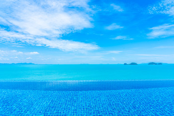 Beautiful luxury outdoor infinity swimming pool with tropical sea ocean and white cloud blue sky background