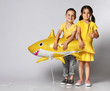 © FAB.1 - Positive young children hold a balloon in the shape of a yellow shark fish, celebrate the holiday, smiling widely, stand on a light background, are in a good mood.