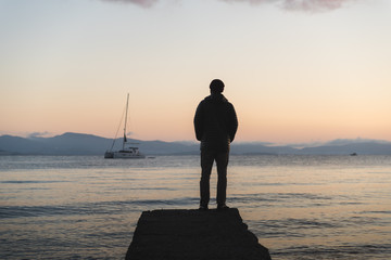 A man standing on a dock during sunrise on Kos, Greece with a boat in the background. 