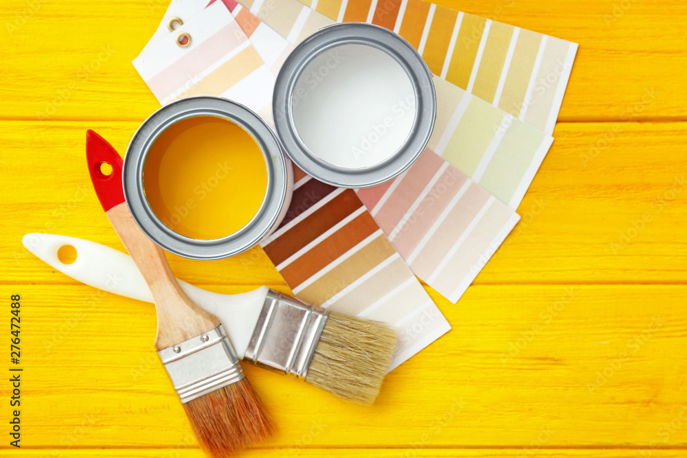 Cans of paint with brushes and palette samples on wooden background