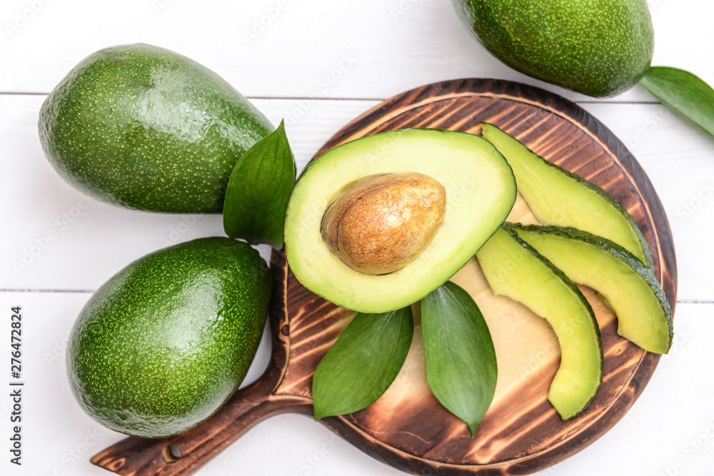 Board with fresh ripe avocados on white wooden background