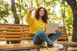 © Drobot Dean - Smiling cheerful young beautiful curly student girl sitting outdoors in nature park using laptop computer.