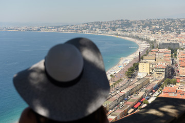 Wall Mural - Nice, France - June 19, 2019: Woman in a hat looks at the beach and promenade of Nice.