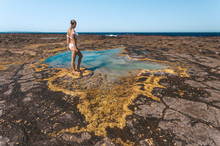 Woman Stands By A Small Rock Pool Edged With Yellow Seaweed