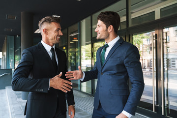 Poster - Portrait closeup of two joyful businessmen partners shaking hands outside job center during working meeting