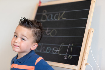 Portrait of little Spanish elementary school pupil with text of Back To School on the blackboard .