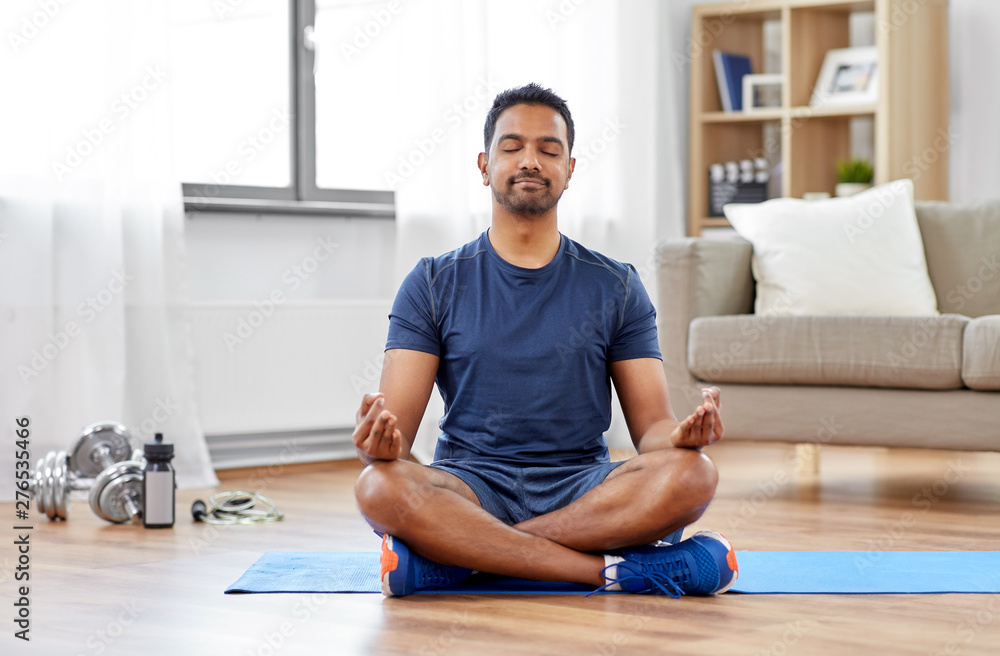 fitness, meditation and healthy lifestyle concept - indian man meditating in lotus pose on exercise mat at home - obrazy, fototapety, plakaty 