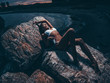 © maksimvostrikov - Sensual, sexy young girl with a seductive slim shapely body in a swimsuit is lying and posing on the rocks at night. Summer dark outdoor photoshoot ashore. Photo on the beach near the sea at twilight