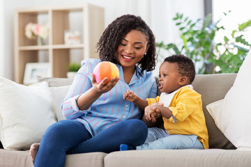 childhood, kids and people concept - happy african american mother and her baby son playing with ball together on sofa at home