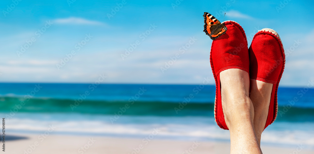 Beine mit roten Stoffschuhen vor Strand und Meer - obrazy, fototapety, plakaty 