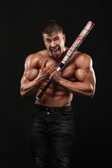 Wall Mural - Brutal strong muscular bodybuilder athletic man pumping up muscles with baseball bat on black background.