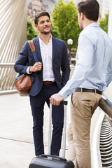 Wall Mural - Happy young two friends colleagues business men standing outdoors talking with each other.