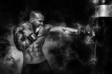 Wall Mural - Sportsman man boxer fighting in gloves with boxing punching bag on dark background with smoke. Copy Space. Black and white photo.