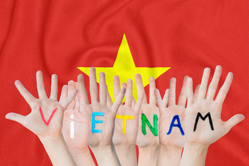 Inscription Vietnam on the children's hands against the background of a waving flag of the Vietnam